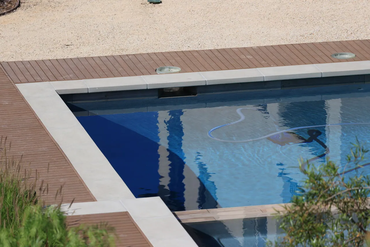 A backyard pool from above with a vacuum hose on the floor.