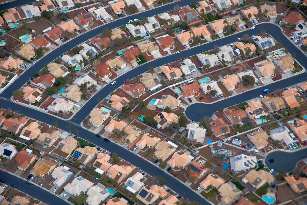 Aerial view of a Las Vegas subdivision with curving streets, tile roofs and small backyard pools behind many of the homes.